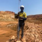 Topographe tenant une canne GNSS et son carnet électronique dans la fosse à ciel ouvert de la mine de Nampala