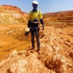 Topographe équipé d'un récepteur GNSS sur un tas de matériau abattu, devant les gradins de la fosse